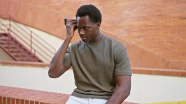 Afro-Amerikalı bir adam şehir merdivenlerinde akıllı telefon kullanıyor, günlük kıyafetler giyiyor, odaklanmış ve yalnız..