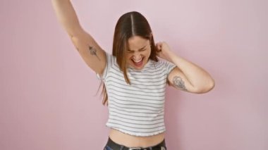 Mavi gözlü genç bir kadın, pembe izole bir arka planda muzaffer duruyor. Heyecan verici bir şekilde sevinç çığlıkları atarak, kazanan hareketi, heyecan verici iş başarısını kutluyor..