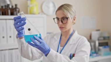 Odaklanmış bir kadın bilim adamı laboratuvarda mavi sıvıyı analiz ediyor..