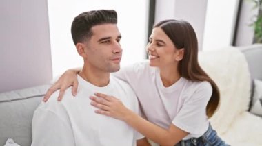 Gülümseyen bir kadın, modern bir oturma odasındaki rahat bir kanepede bir erkeği kucaklıyor. Aşkı ve birlikteliği tasvir ediyor..