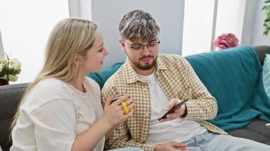 Rahat bir oturma odasında sıradan bir çift, elinde kahve fincanı tutan bir kadın ve akıllı telefon kullanan bir adam..