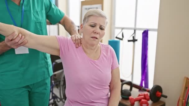 理学療法クリニックでは 女性患者は肩のリハビリテーション演習で男性セラピストと協力します — ストック動画