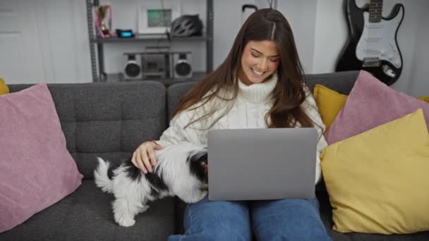 一个笑着的女人坐在沙发上 拿着笔记本电脑 在舒适的客厅里摸着她的小猎犬 — 图库视频影像