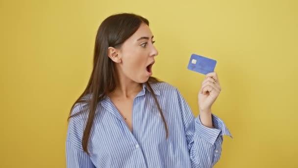 驚くべき若いヒスパニック女性 ショックと不信感で口を開き 彼女の孤立した黄色の背景を怖がらせてクレジットカードをクラッチ — ストック動画