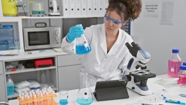 一位年轻的惊慌失措的女科学家在实验室里检查瓶子里的蓝色液体 — 图库视频影像