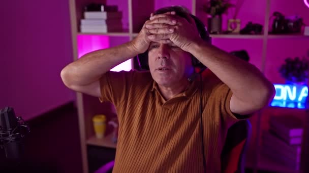 在霓虹灯照明的游戏室内 一个头戴耳机的紧张男人表示沮丧或精疲力竭 — 图库视频影像