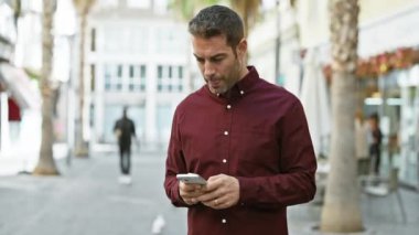 Şehir caddesinde akıllı telefon kullanan sakallı yakışıklı bir İspanyol.