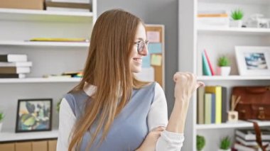 Heyecanlı, kendine güvenen genç sarışın iş kadını seni ve kamerayı zevkle işaret ediyor. Olumlu bir şekilde gülümsüyor, iş yerinin rahatlığında..