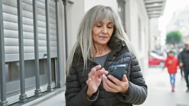 Şehir caddesinde akıllı telefondan mesaj atan orta yaşlı bir kadın, çağdaş şehir yaşam tarzını yansıtıyor..