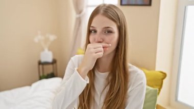 İlginç bir sır, pijamalı genç sarışın kadın, fermuarını kapatıyor, yatak odasında oturuyor. sessiz ve yasak dedikodu kavramı