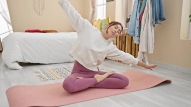 Genç bir kadın dingin yatak odasında pembe bir yoga minderine uzanıyor. Huzur ve sükuneti somutlaştırıyor..