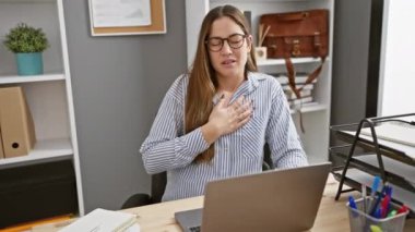 Modern ofis ortamında rahatsızlık duyan bir kadın göğsüne sarılıp sıkıntılı görünüyor..