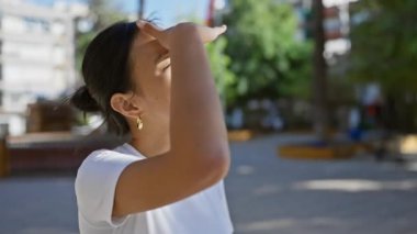 Genç Asyalı kadın, güneşli şehir sokağına bakarak, gözleri gölgede bırakıyor.