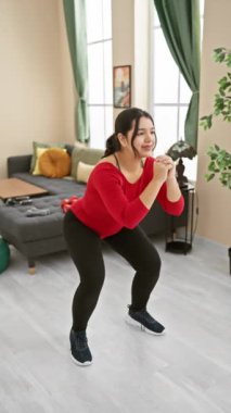 Gülümseyen genç bir İspanyol kadın spor giysileri içinde geniş bir salonda egzersiz yaparken esniyor..