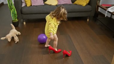 Meraklı sarışın bir çocuk rahat bir oturma odasında kırmızı topuklu ayakkabı deniyor. Yanında peluş bir oyuncak ve mor bir top var. Evdeki masumiyeti simgeliyor..