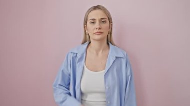 Şok olmuş genç bir kadın elleriyle yüzünü kapatıyor, parmaklarının arasından dikizliyor. Pembe izole edilmiş arka planda tişörtlü sarı saçlı güzel. Utanç ve şaşkınlık dolu utangaç bakışlar..