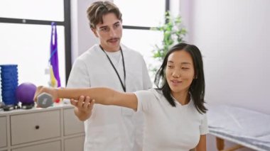 Fizyoterapist hasta kadına terapi odasında halterli rehabilitasyon egzersizinde yardım ediyor..