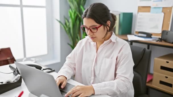 若いヒスパニック系女性がオフィスの設定でノートパソコンで作業中に胃痛を経験する — ストック動画