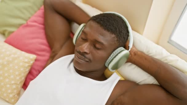 Rahat Afrikalı Bir Adam Renkli Bir Yatak Odasında Kulaklıkla Müzik — Stok video