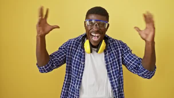 兴奋的非洲裔美国人 戴着安全眼镜 站在那里疯狂 疯狂地胜利举起双臂 喜悦地庆祝他因孤独的黄种人背景而获胜 — 图库视频影像