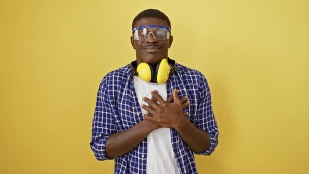誇らしげに立って スポーツの安全眼鏡 微笑み 健康ジェスチャー 隔離された黄色の背景の胸に手を表示する感謝するアフリカ系アメリカ人男性 — ストック動画