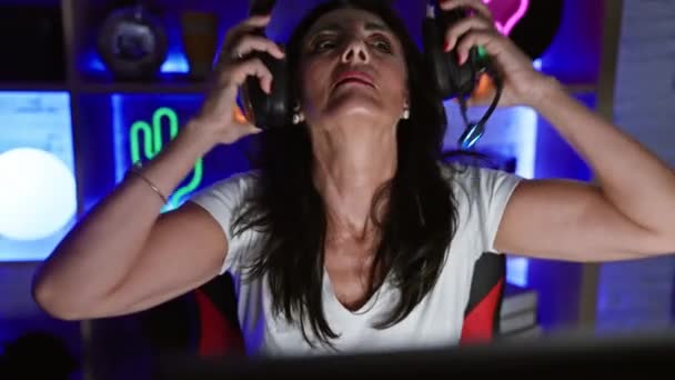 一个成熟的女人晚上带着耳机 电脑和五颜六色的彩灯在屋里玩游戏 — 图库视频影像