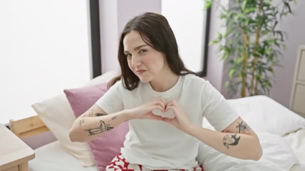 Wesoła Młoda Kobieta Piżamie Siedzi Łóżku Tworząc Symbol Serca Dłońmi — Wideo stockowe
