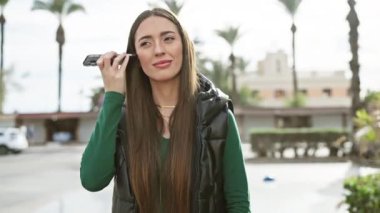 Şehir ortamında kulaklıkla akıllı telefon kullanan gülümseyen kadın..