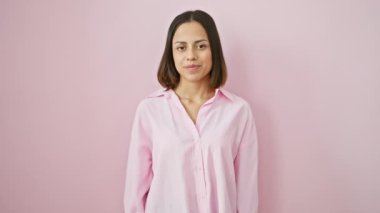 Kolları açık duran neşeli, genç İspanyol bir kadın. Pembe arka planda gülümsüyor.