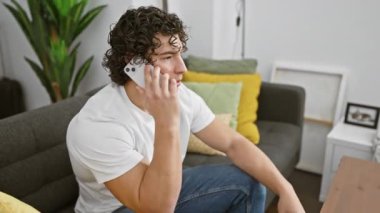 Modern bir oturma odasında, kıvırcık saçlı, akıllı bir telefonla konuşan genç bir İspanyol..