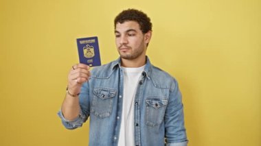 Şok olmuş genç bir Arap adam, eliyle ağzını kapatıyor, emirlik pasaportu tutuyor, şaşırmış bir ifade sergiliyor, beklenmedik bir hata yapmaktan korkuyor. sarı arkaplanda izole.