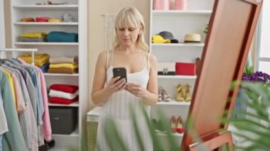 Renkli kıyafetler ve ayakkabılarla dolu bir dolapta akıllı telefon kullanan sarışın kadın..