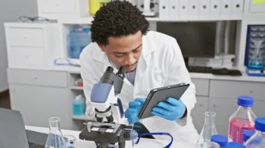 Bir laboratuarda mikroskopla çalışırken, bir tablet üzerindeki verileri analiz eden Afrikalı Amerikalı erkek bilim adamı..