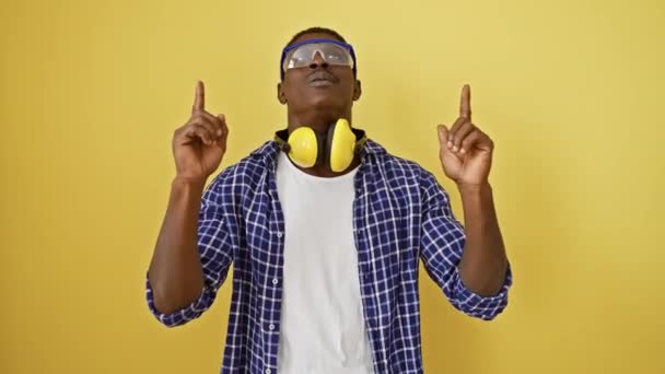 安全眼鏡をかけたアフリカ系アメリカ人が驚き 指摘し 驚いた 明るい黄色の隔離された背景に一人で立って 肯定的なバイブを放射する — ストック動画