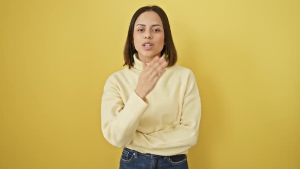 セーターで美しい若いヒスパニックの女性は カメラに向かってキスを吹き飛ばし 愛と前向きさを表現します 黄色の背景に隔離された — ストック動画