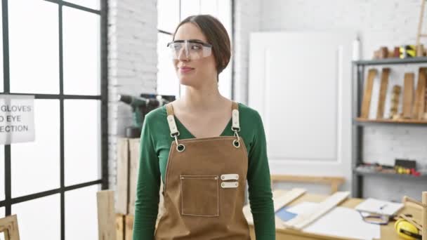 ワークベンチによる安全ガラスとエプロンを備えた木工スタジオで自信を持った女性 — ストック動画