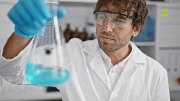 Ein Fokussierter Mann Laborkittel Untersucht Labor Blaue Flüssigkeit Becher — Stockvideo