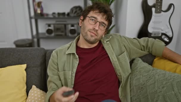 수염과 안경을 편안한 남자는 아늑한 거실에서 소파에 리모컨을 — 비디오