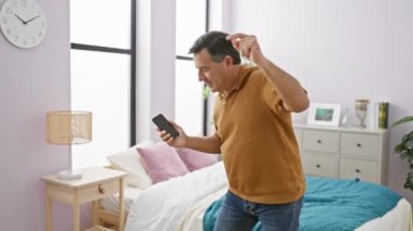 İyi ışıklandırılmış şık bir yatak odasında akıllı telefon kullanan orta yaşlı bir adam duygularını ifade ediyor..
