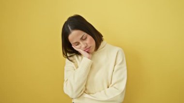 Depresyondaki genç İspanyol kadın, yorgun görünüyor, sorunlarını düşünüyor, kederle maskelenmiş güzel yüzünü sıkıyor, kazak giyiyor, kollarını kavuşturuyor, izole edilmiş sarı duvara karşı duruyor.