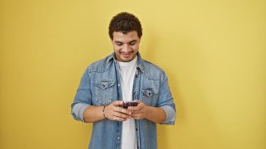 Muzaffer genç Arap adam, neşeli zaferini mutlu bir gülümsemeyle kutluyor. Kazanan kutlama, başarı sevinci telefonu kullanmak, sarı arka planda tek başına durmak..