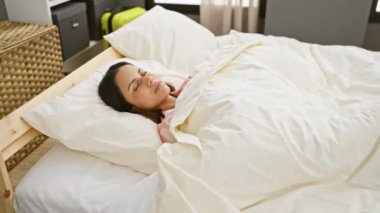 Genç bir İspanyol kadın yatak odasında uyanıyor, enerjik bir gülümsemeyle esniyor, enerji ve refah duygusu taşıyor..