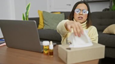 Genç bir kadın, evde dizüstü bilgisayarında çalışırken hapşırıyor yanında grip ilacı ve bir kutu mendille, bu da genel bir hastalık günü senaryosunu yansıtıyor..