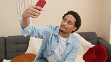 Yakışıklı adam rahat bir oturma odasında akıllı telefonuyla selfie çekiyor.
