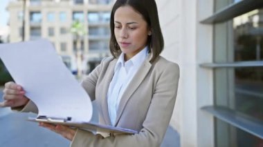 Kendine güvenen İspanyol iş kadını, güneşli bir şehir caddesindeki belgeleri inceliyor.