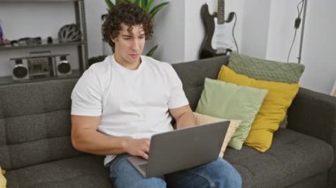 Kıvırcık saçlı neşeli, genç İspanyol adam evinde online zaferini kutluyor! Neşeli bir anda yakalandı, koltuğuna oturdu, dizüstü bilgisayarı kucağında, zaferle elini kaldırdı..