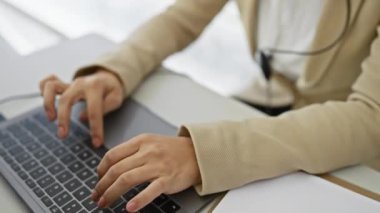 Kulaklıklı, parlak bir ofis ortamında dizüstü bilgisayara odaklanmış İspanyol bir kadın..