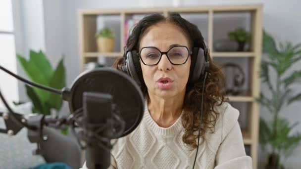 在室内的收音机演播室里 戴耳机对着话筒说话的中年妇女 — 图库视频影像