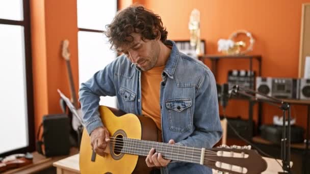 幸せなヒスパニックの男は 魅力と音楽の才能を誇る活気に満ちた音楽スタジオでアコースティックギターを演奏します — ストック動画