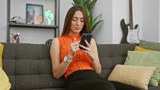 Uma Mulher Uma Blusa Laranja Desfruta Seu Smartphone Sofá Com — Vídeo de Stock